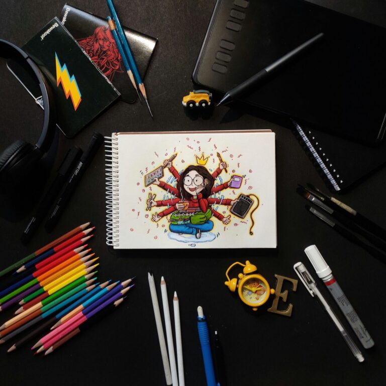 Flat lay of a graphics tablet and stylus beside a sketchbook, colored pencils and headphones
